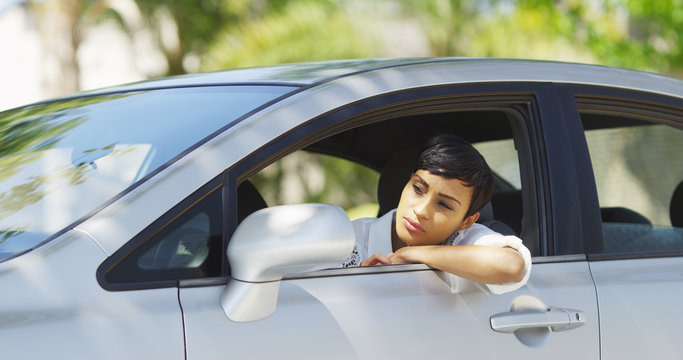 Black woman in car looking around and checking hair in mirror