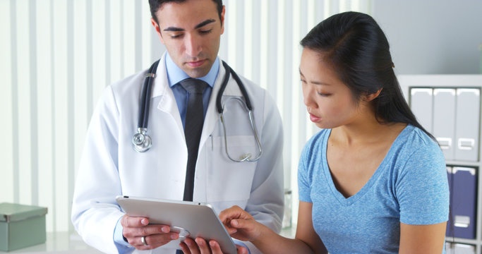 Hispanic Doctor Talking With Patient With Test Results On Tablet