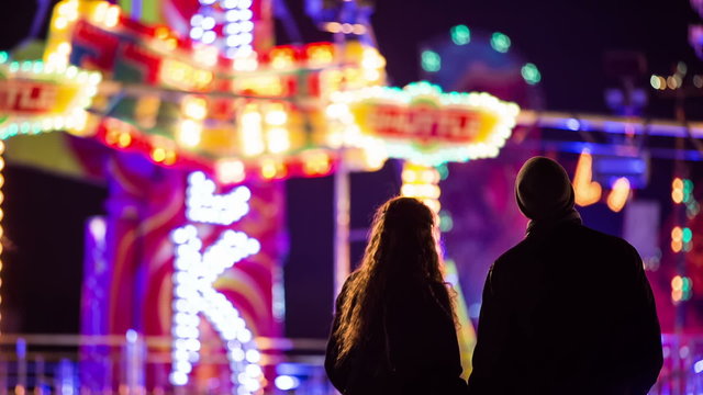 Couple watching people on amusement ride at night