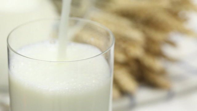 Pouring milk into glass on table with agricultural products in the back