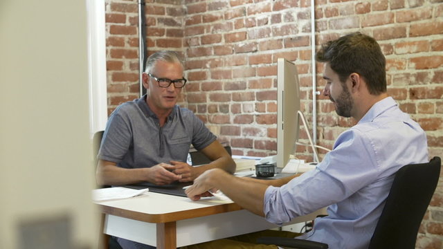 Older Businessman Interviewing Male Job Applicant In Office