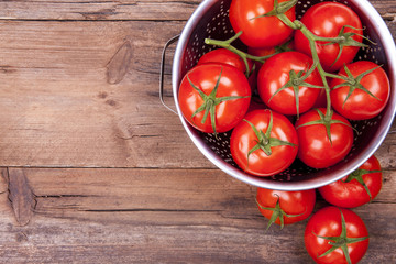 Bunch of tomatoes on vine in colander and out of it shot from above with negative space on a wooden...