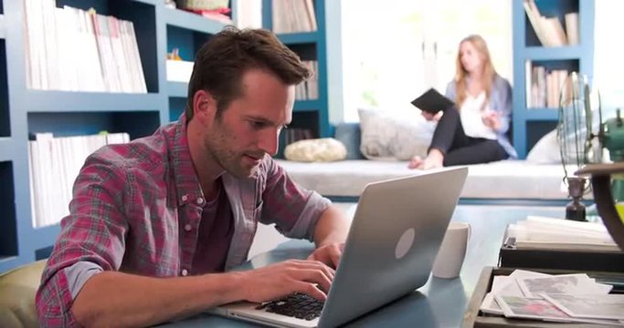 Couple In Home Office Using Laptop And Digital Tablet