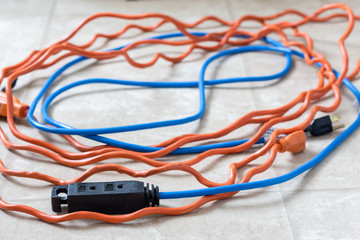 horizontal image of two long  blue and orange extension cords lying tangled up on the floor.