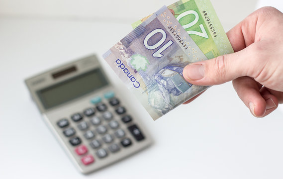 horizontal image of a hand holding a 20 and a 10 dollar canadian bill with  calculator blurred on white background