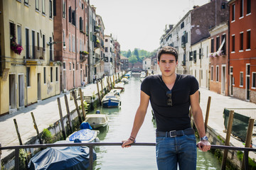 Fototapeta na wymiar Young Man on Bridge Over Narrow Canal in Venice