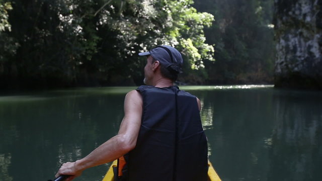 man backside view rows on kayak in canyon	