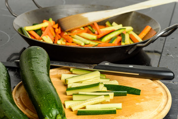 Cooking of stir-fried vegetables with zucchini and carrots. Focus on cutting board in foreground