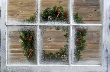 Fototapeta na wymiar Snow covered window with decorative Christmas wreath on window