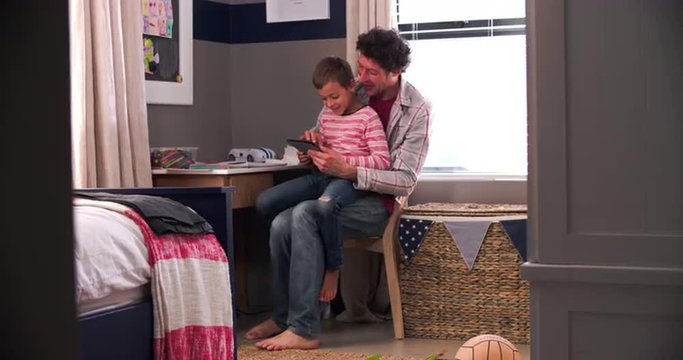 Father And Son Sitting In Bedroom Using Digital Tablet