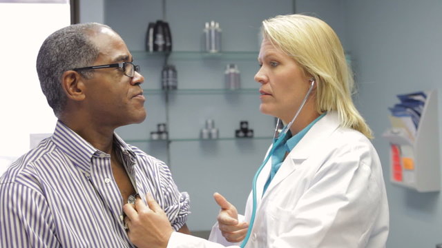 Doctor Listening To Male Patient's Chest With Stethoscope