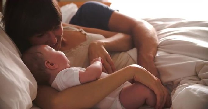 Parents Lying In Bed Cuddling Baby Daughter 