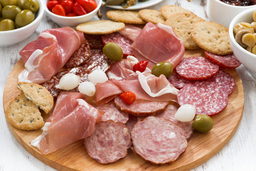 Assorted meat snacks, sausages and pickles on wooden board