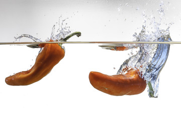 Due rossi peperoni cdono in acqua con un grande splash , bolle d'aria e schizzi. Sfondo bianco