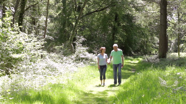 Senior Couple Walking Along Summer Woodland Path Together