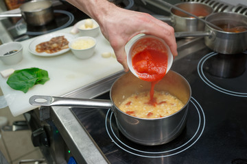 Chef is adding tomatoes to risotto