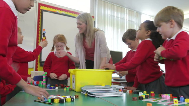 Pupils And Teacher Tidying Up Coloured Blocks