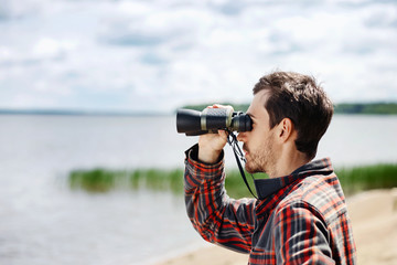 Obraz premium Man looks through binoculars while fishing at the lake on vacati