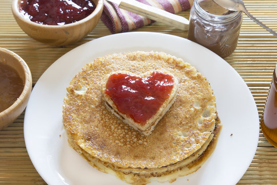 Heart shaped pancake with strawberry jam on stack of pancakes