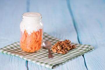 Yogurt with carrot in a glass jar on a napkin. Walnuts. Blue background.