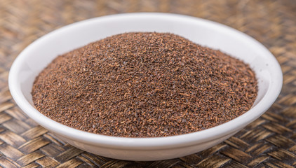 Dried processed tea leaves in white bowl over rustic wicker background