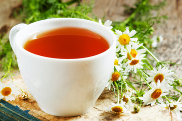 cup of black tea, wild chamomile, old books on wood background,