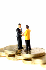 Miniature businessmen handshake pound coins.
Miniature scale model businessmen shaking hands on British pound coins.