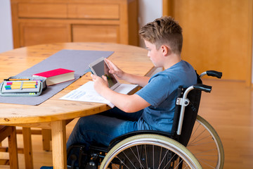 boy in wheelchair doing homework and using tablet pc