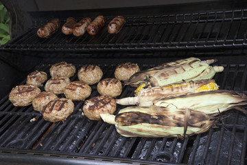 Food cooking on a gas barbecue. Sausages,turkey burgers and corn