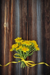 Bouquet from yellow daisy with yellow satin ribbon on wooden bac