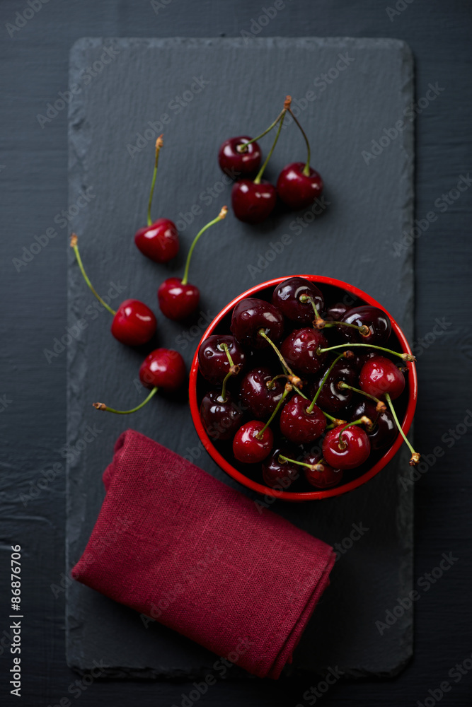 Wall mural Stone slate plate with sweet cherries, top view, studio shot