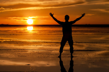 Fototapeta premium Silhouette si un uomo a braccia aperte nel salar de Uyuni , Bolivia . Tramonto e riflessione del sole e della luce sulla superficie bagnata del sale