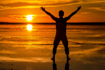 Fototapeta premium Silhouette si un uomo a braccia aperte nel salar de Uyuni , Bolivia . Tramonto e riflessione del sole e della luce sulla superficie bagnata del sale