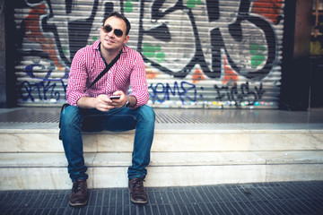 Portrait of handsome man with phone in hand, casually dressed with shirt, jeans and sunglasses...