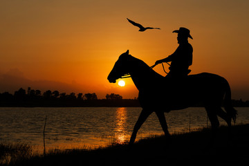 silhouette of Cowboy sitting on his horse at river full moon after sunset background
