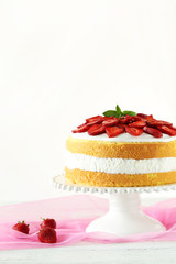 Sweet cake with strawberries on cake stand on white wooden backg