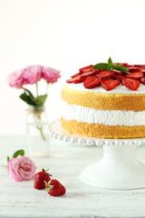 Sweet cake with strawberries on cake stand on white wooden backg