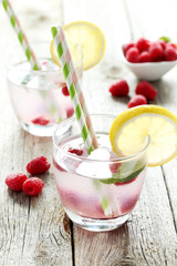 Raspberries and juice in glass on grey wooden background