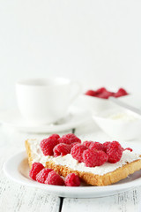 Fresh toast with cream cheese and raspberries on white wooden ba