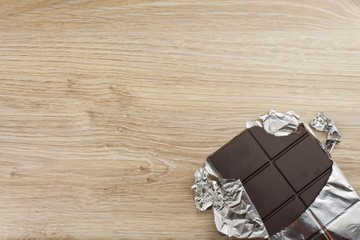 Chocolate wrapped in aluminum foil on a wooden board. Wrapped sweet treat.
