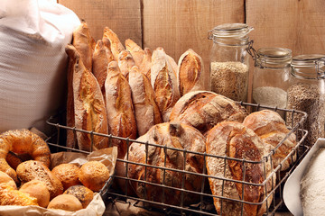 Fresh bread in metal basket in bakery on wooden background