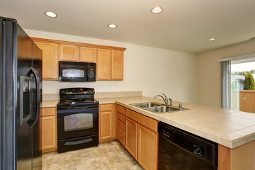 Fototapeta premium Mała kuchnia z podłogą wyłożoną kafelkami i czarną lodówką.