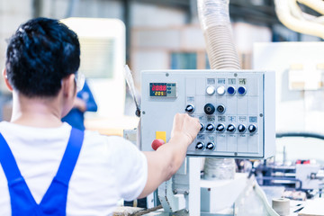 Worker pressing buttons on CNC machine in factory