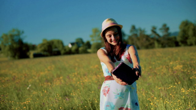 Girl standing on the meadow and doing selfie on tablet
