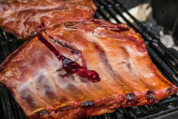Pork Ribs on Grill. Charcoal outdoor BBQ grill with pork ribs cooking and being smoked. Some blood visible.