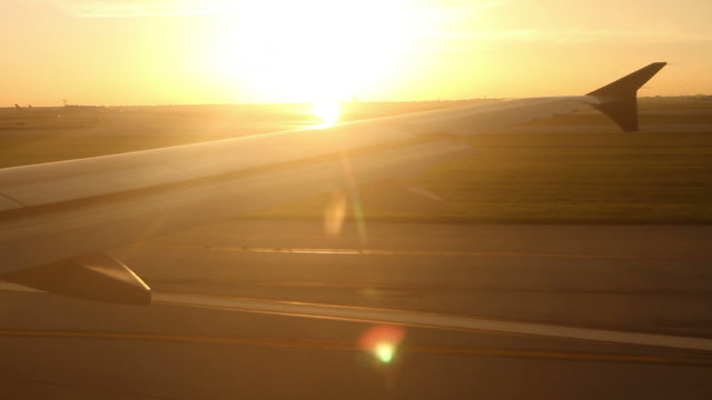 Plane Takeoff at Sunset – Looking out the window at the wing of a jet as it takes off the runway, with a brilliant sunset in the distance