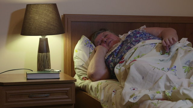  Obese senior woman talking on the phone lying on bed in bedroom