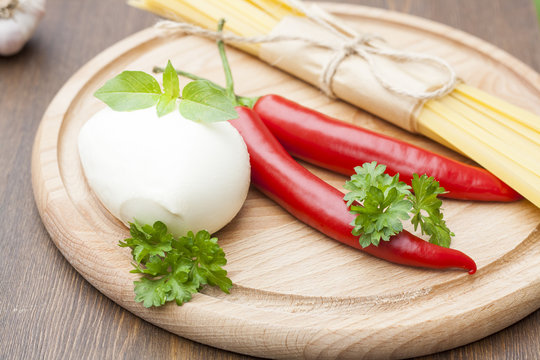 Mozzarella with herbs, noodles, chilli, on a wooden round board, selective focus