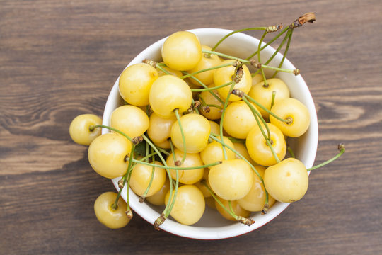 Fresh yellow cherry in a red bowl on a wooden background, selective focus
