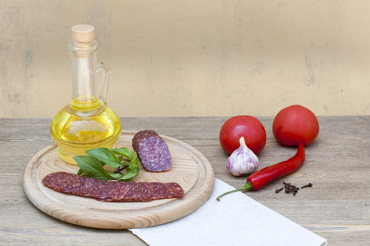 Salami sausage and sunflower oil in the bottles with herbs, tomatoes and spices on wooden table, selective focus